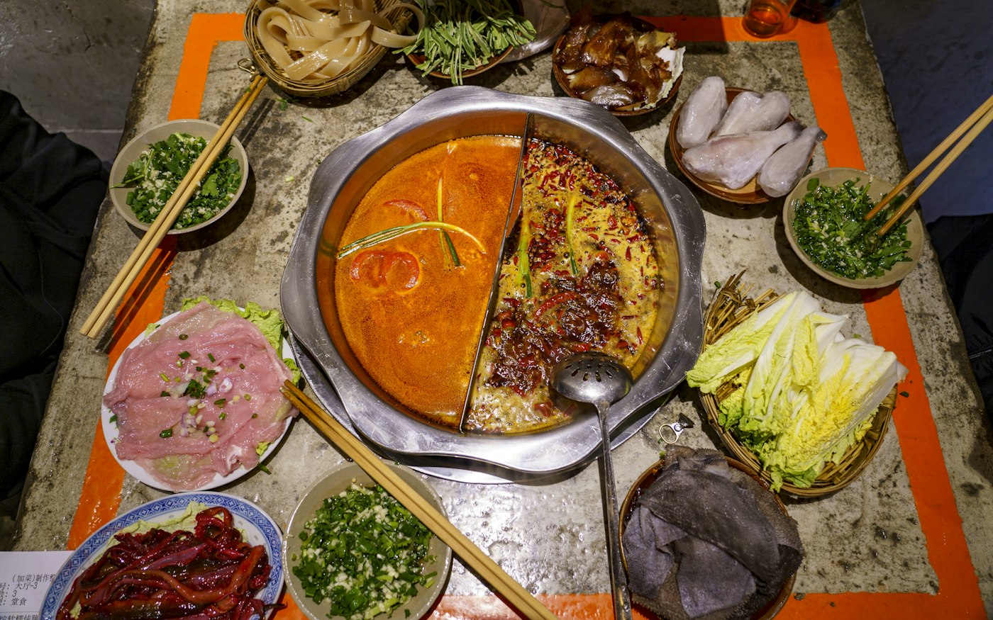 A split hot pot of spicy and clear broth among plates of meat and vegetables