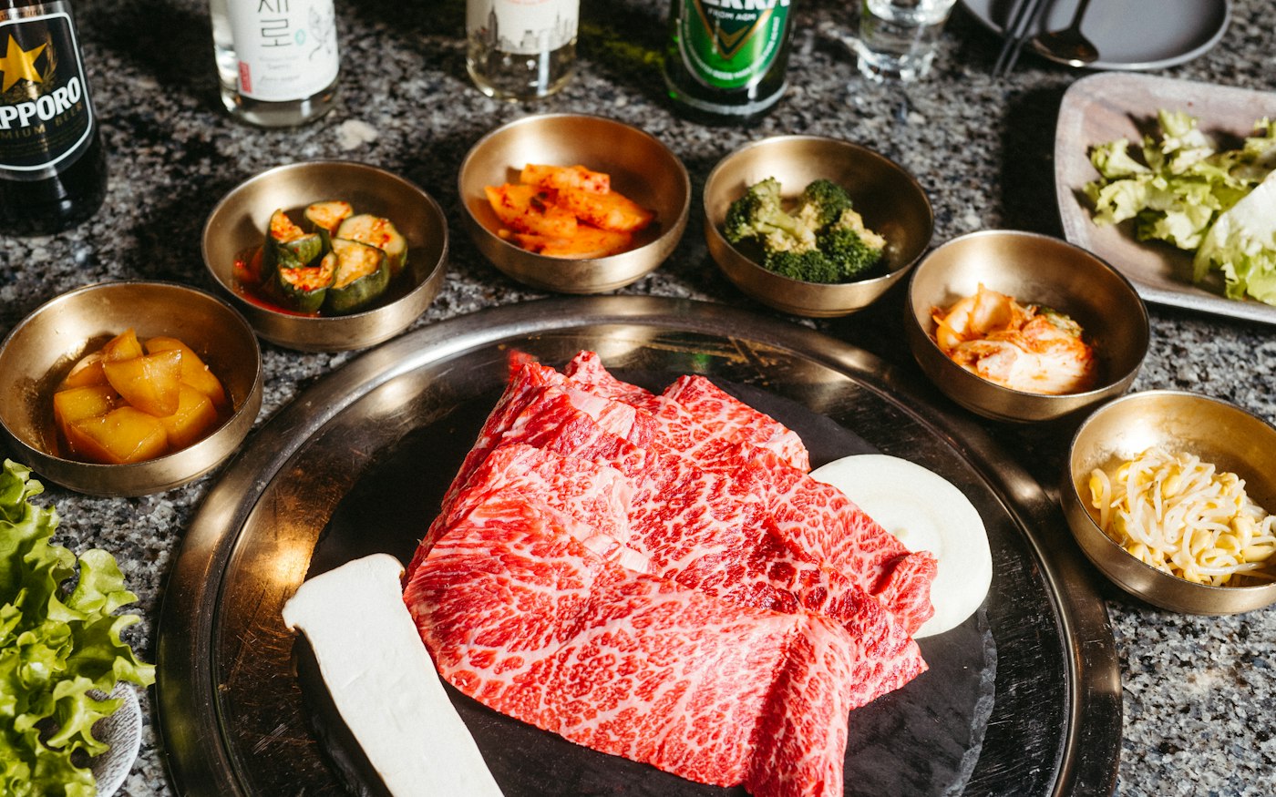 Marbled beef on a tabletop grill ringed by banchan
