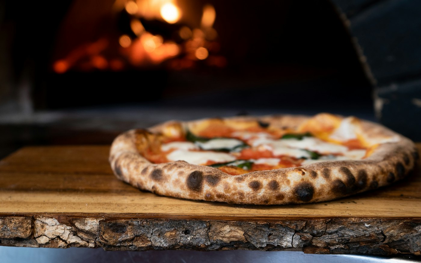 A blistered pizza in front of a wood-fired oven